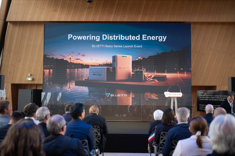 Audience seated facing projection screen displaying 'Powering Distributed Energy' presentation with distributed energy equipment imagery