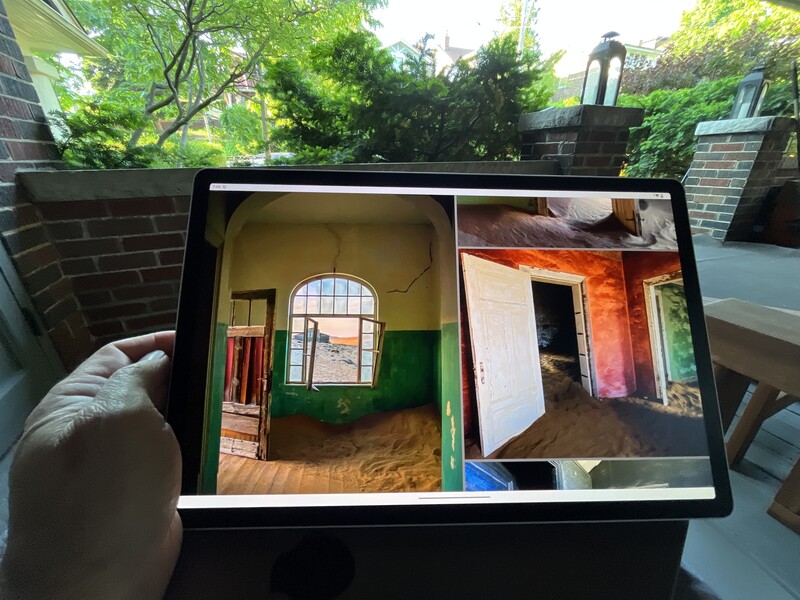 Tablet displaying two interior room photographs side by side, held in outdoor garden setting