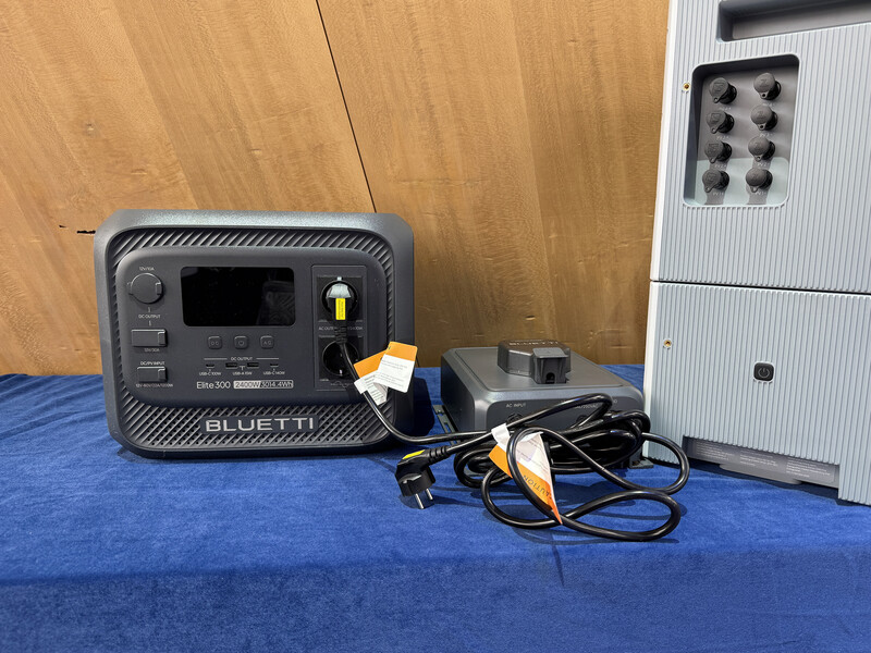 Bluetti portable power station with charging cables on blue surface next to white equipment rack