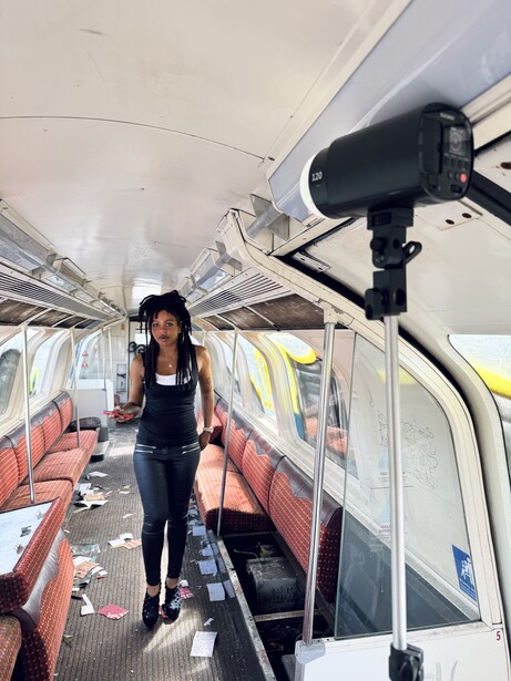 Woman standing in empty passenger train car with red seats and overhead camera mounted on ceiling