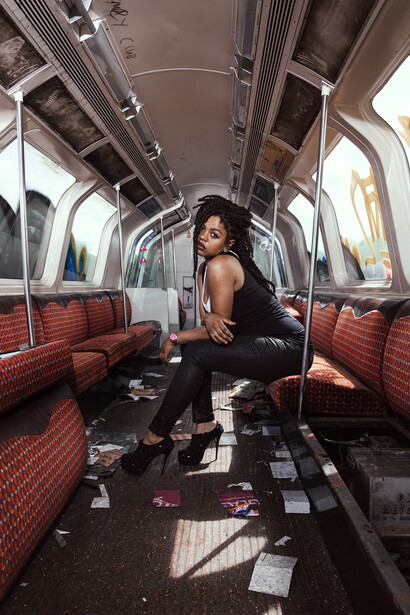 Woman in black tank top posing inside a vintage train car with red seats and natural window light