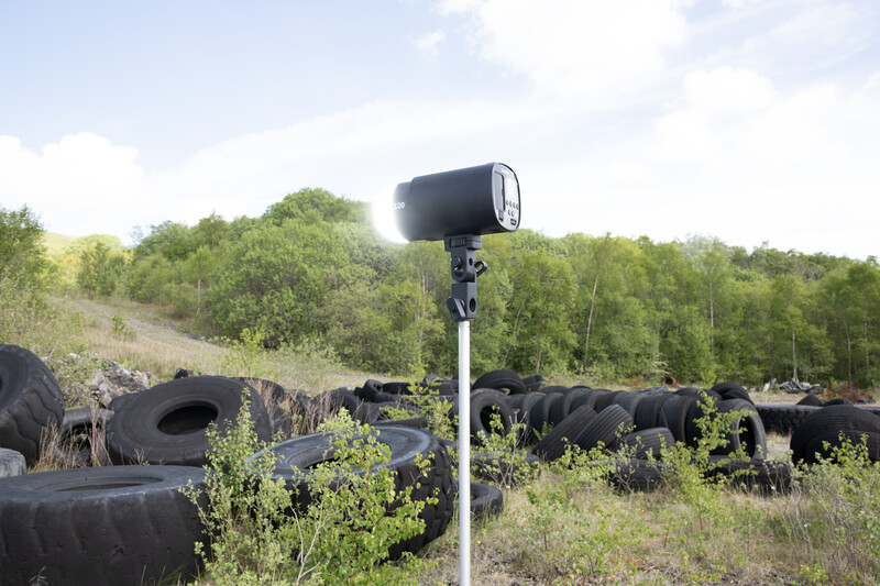 Discarded black tires scattered across overgrown hillside with blue survey equipment pole in foreground