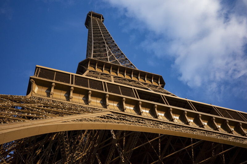 Upward view of the Eiffel Tower's iron lattice structure against blue sky with white clouds