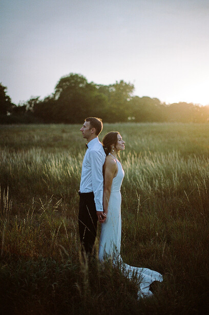 Couple in formal attire standing in a golden-hour backlit field with soft-focus trees