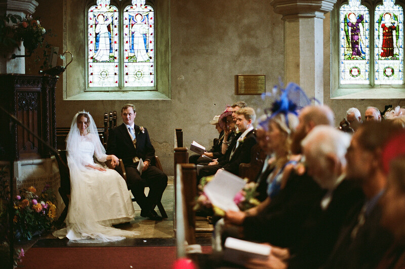 Bride and groom kneeling at altar during church ceremony with guests blurred in foreground