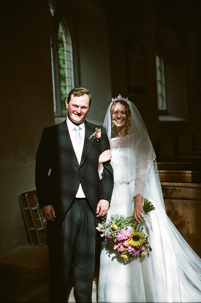 Bride and groom in formal wedding attire posing in a church interior with stained glass windows