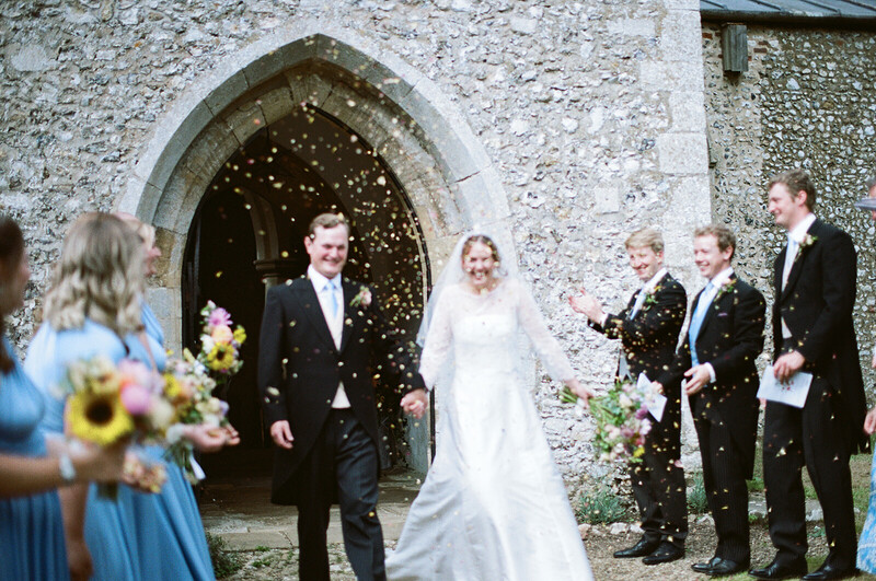 Bride and groom exiting stone church as guests toss confetti