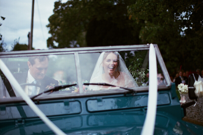 Bride in white veil in vintage convertible with groom during wedding day departure