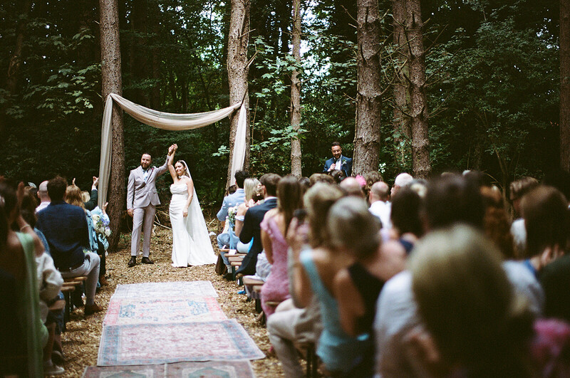 Outdoor woodland wedding ceremony with bride and groom at altar under white fabric arch