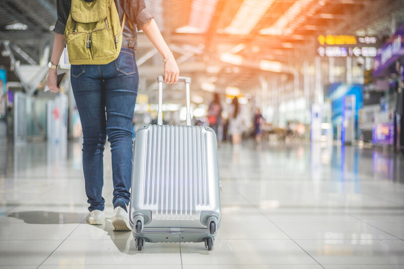 Woman with yellow backpack pulling silver rolling suitcase through airport terminal