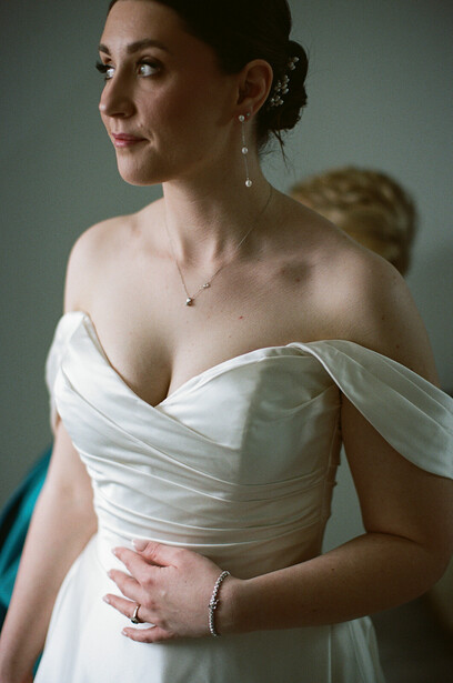 Bride in white draped off-shoulder wedding dress with posed hand placement, studio portrait lighting