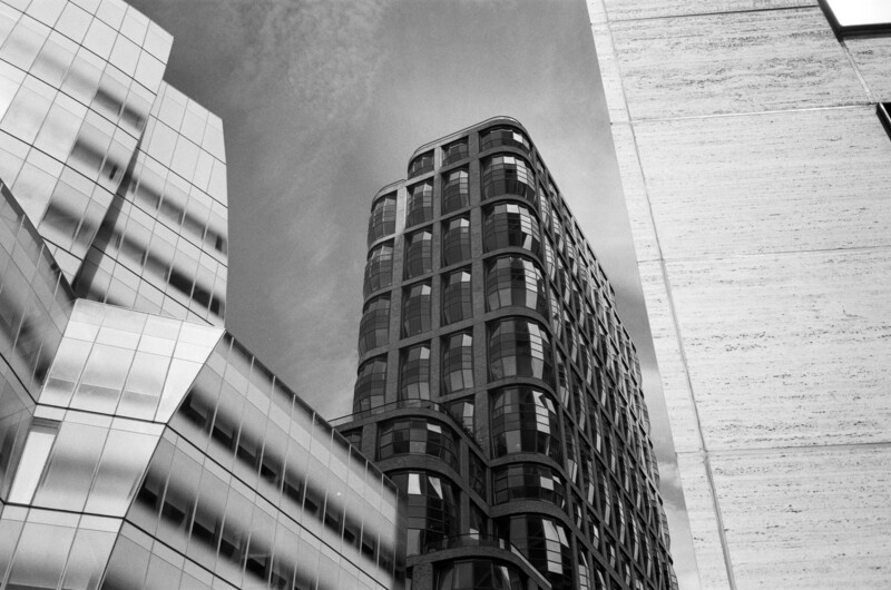 Black and white upward-angle photograph of a curved corner building surrounded by modern architectural structures