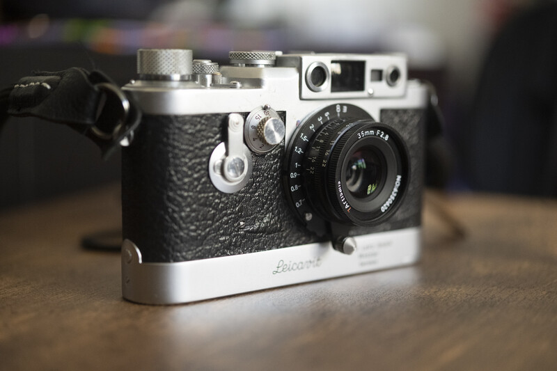 Vintage rangefinder camera with black leather body and chrome accents on wooden surface
