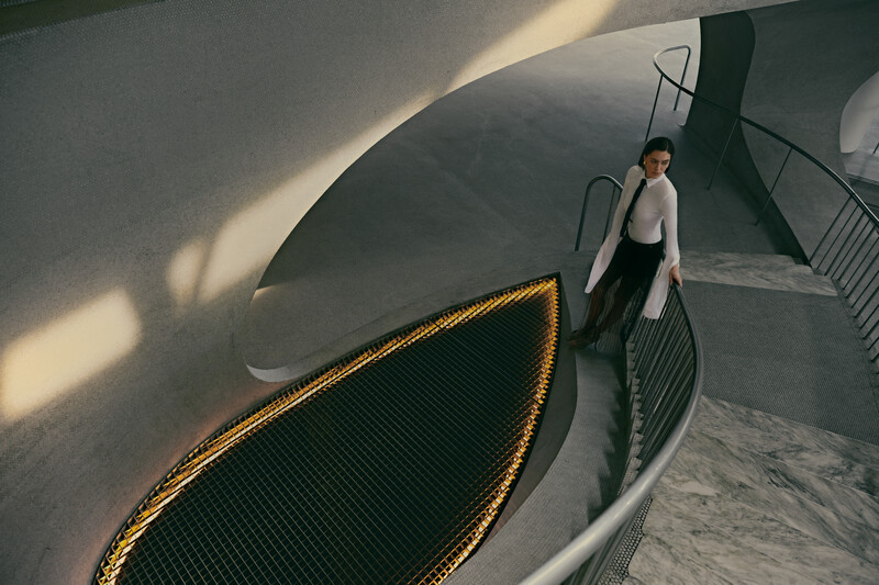 Person in light blazer descending curved staircase with dramatic overhead lighting and shadows