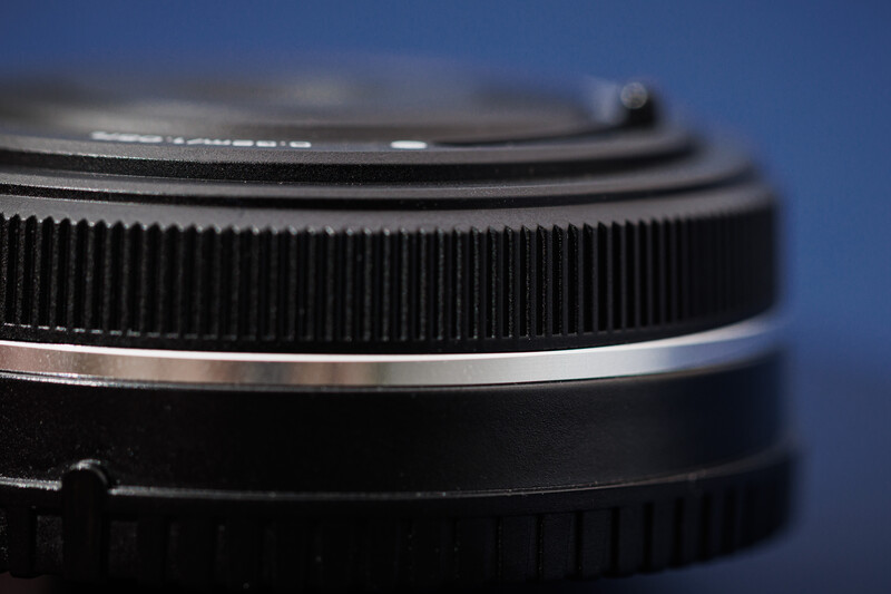 Close-up of camera lens barrel showing focus ring and aperture ring details against blue background