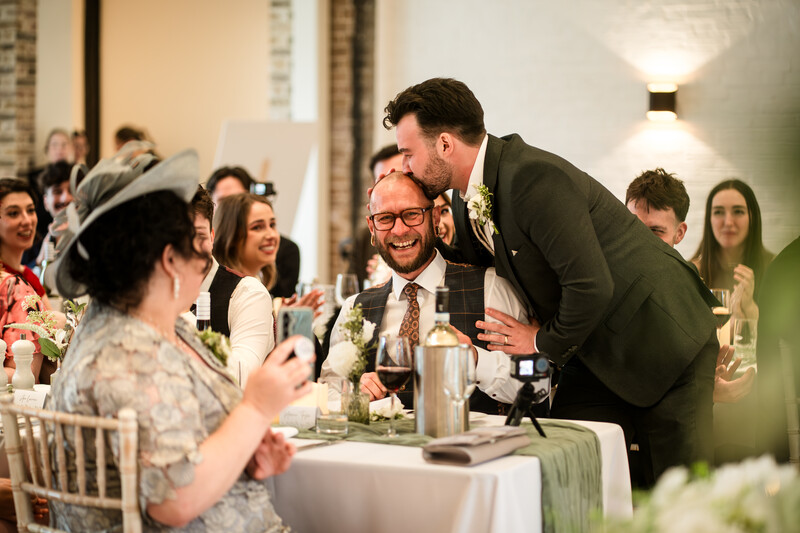Groom leaning over to embrace guest during wedding reception dinner service