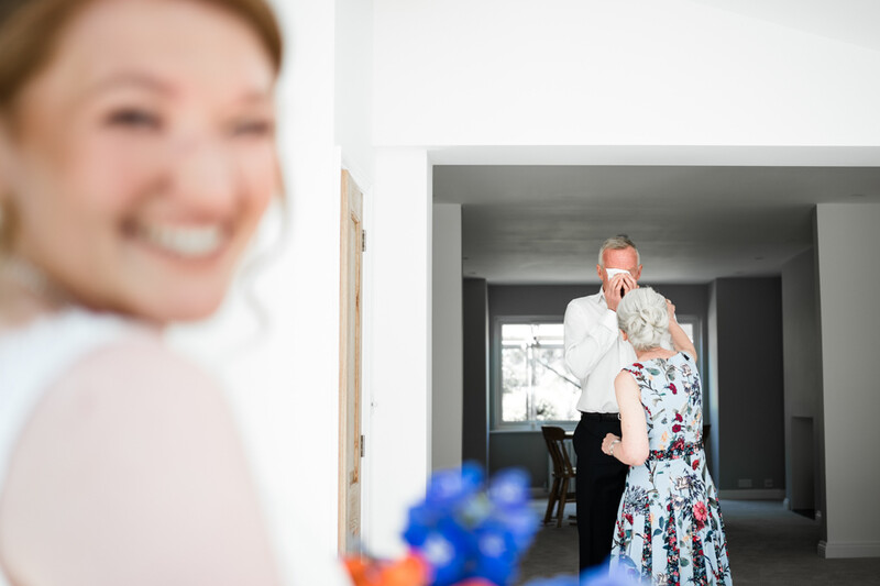 Through-the-door shot of couple embracing in hallway with smiling woman's face in soft focus foreground