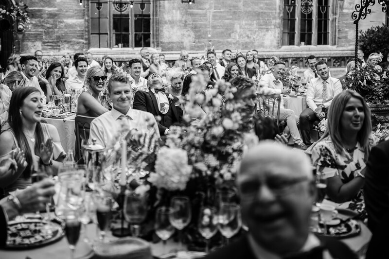 Black and white photograph of outdoor wedding reception with guests seated at long tables adorned with floral centerpieces