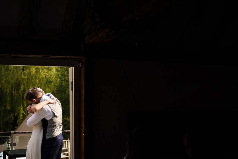 Bride and groom embracing on a sunlit balcony with green foliage visible through the doorway