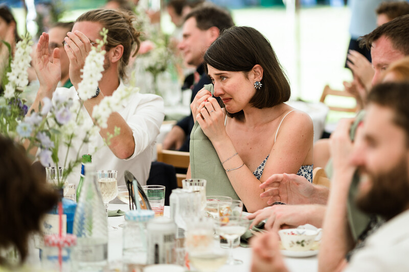 Woman smiling during an indoor dining event with floral centerpieces and multiple guests at a long table