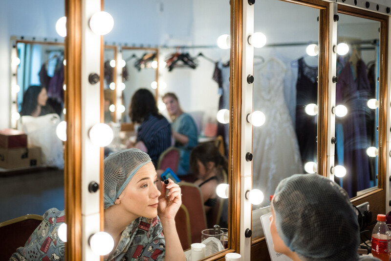 Woman applying makeup at a Hollywood-style vanity mirror with illuminated bulbs