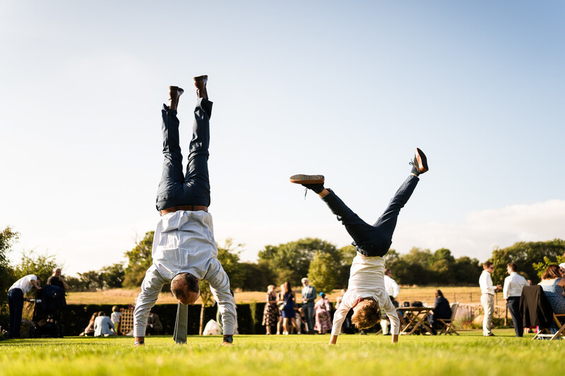 Two people performing handstands on grass at an outdoor event with spectators in background
