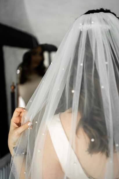 Bride adjusting delicate beaded veil with black headpiece during wedding preparation
