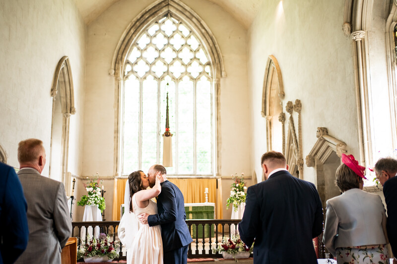Bride and groom kiss at altar in Gothic-style church with pointed arch window