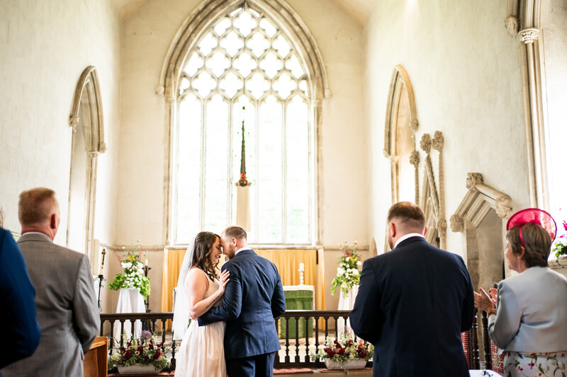 Bride and groom exchanging vows at altar in Gothic church with tall pointed-arch window