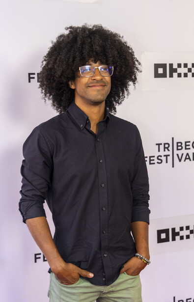 Person wearing sunglasses and black button-up shirt at media event