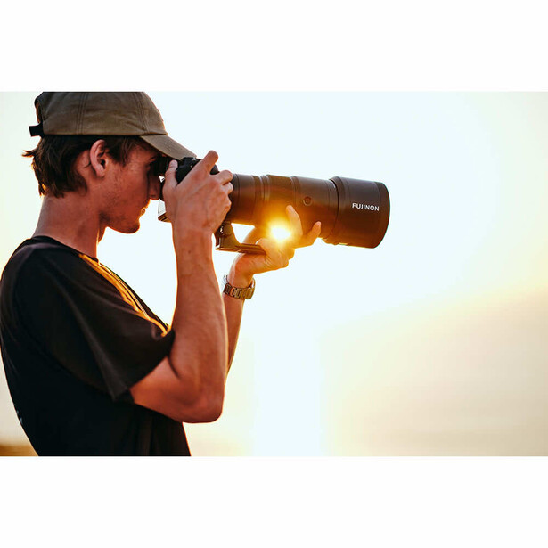 Photographer looking through telephoto lens at golden hour with backlighting