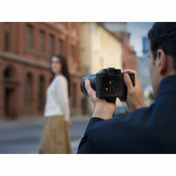 Photographer holding professional camera with rear LCD screen visible, shooting portrait of woman in urban brick setting