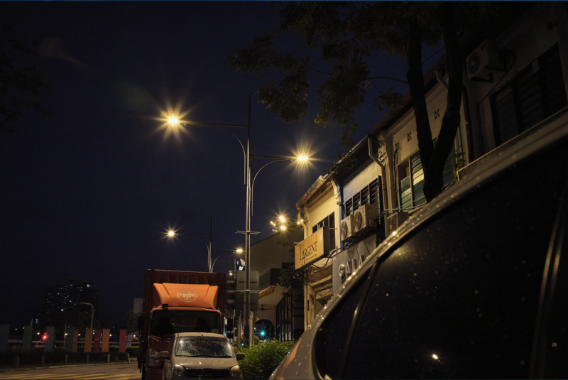 Night street scene with illuminated storefronts and street lamps casting warm light