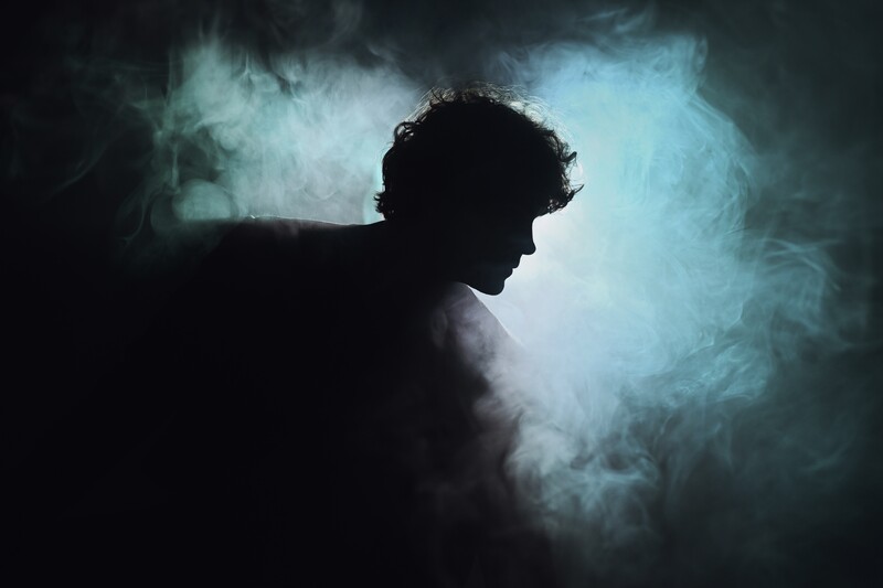 Silhouetted male profile against luminous blue-green atmospheric smoke and light