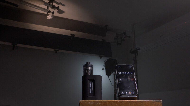 Studio setup with wireless microphone transmitter and smartphone displaying time code on wooden shelf