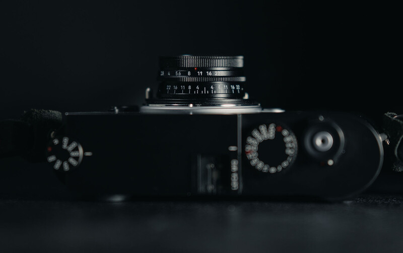 Vintage rangefinder camera with manual focus lens mounted on top, photographed against dark background