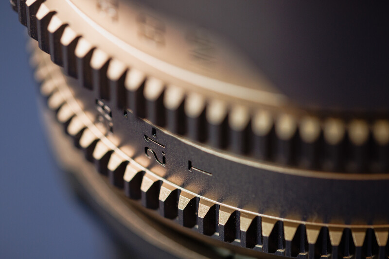 Close-up macro photograph of camera lens gear teeth with selective focus and warm studio lighting