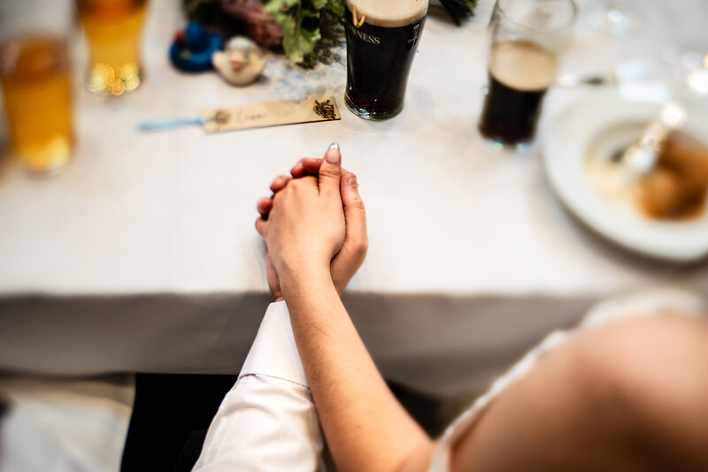 Two hands clasped together on a white table during a meal, with blurred beer glasses and food plates in background