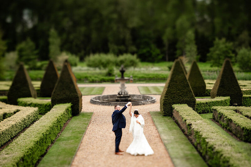 Bride and groom standing in formal garden with geometric hedges and fountain
