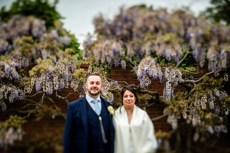 Couple posing together beneath cascading wisteria blooms in soft, natural daylight