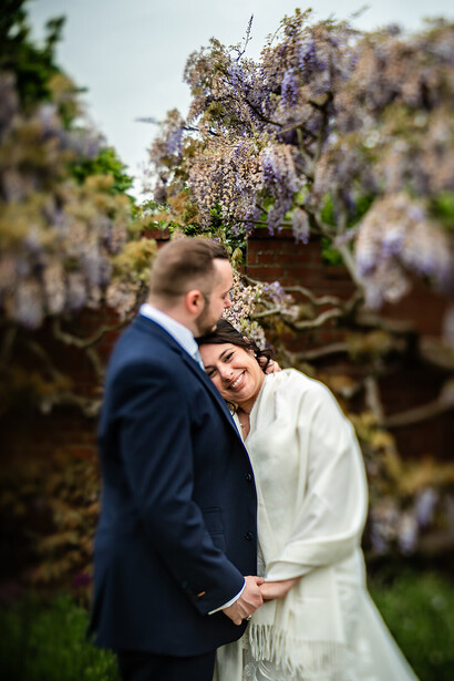 Bride and groom embracing outdoors beneath blooming wisteria vines