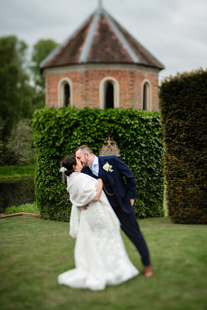Bride and groom pose together on grass with ivy-covered brick tower in background