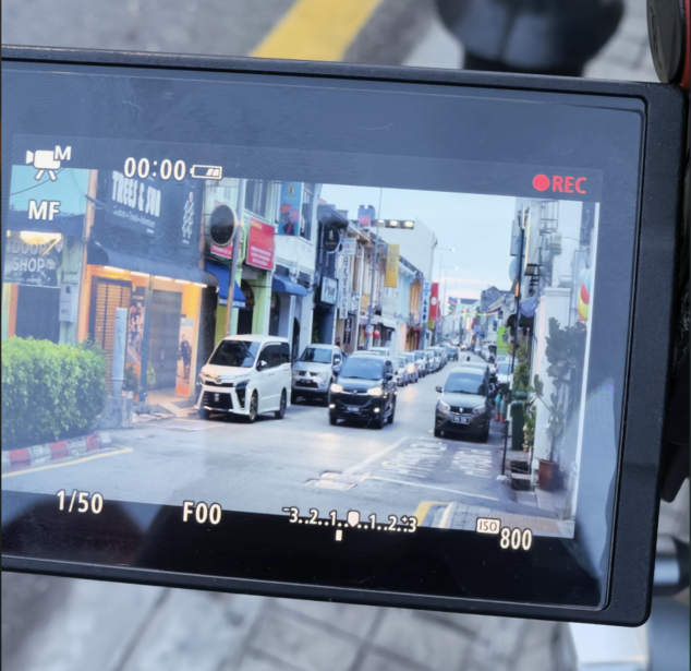 Camera LCD screen displaying live video feed of an urban street scene with vehicles and storefronts