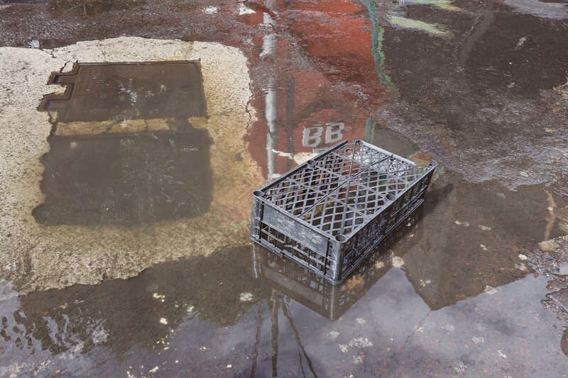 Black plastic crate reflecting in puddle on wet pavement