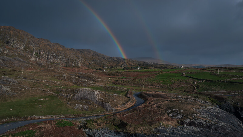 Double rainbow over moorland valley with winding river and scattered buildings