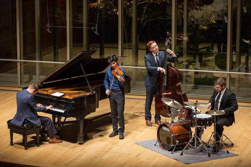 Jazz quartet performing on stage with piano, violin, bass, and drums