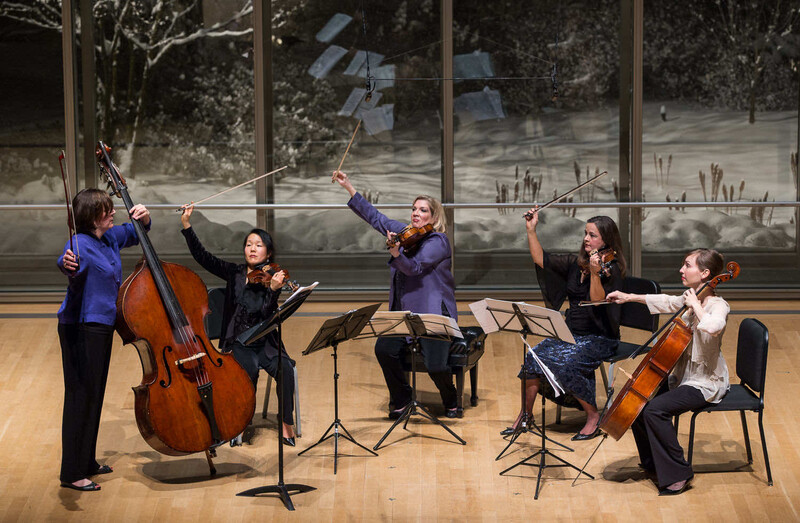 Five classical musicians performing chamber music with string instruments in a concert hall