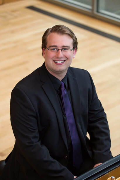 Professional portrait of a smiling man wearing glasses and dark blazer with purple shirt