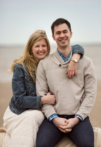 Couple posing together on a beach with overcast sky behind them
