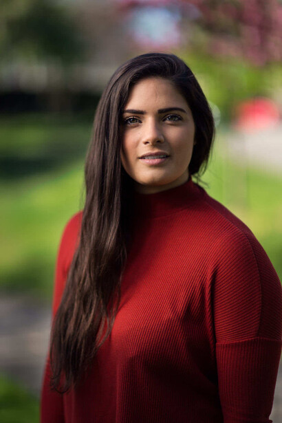 Woman in red sweater with long dark hair looking over shoulder outdoors